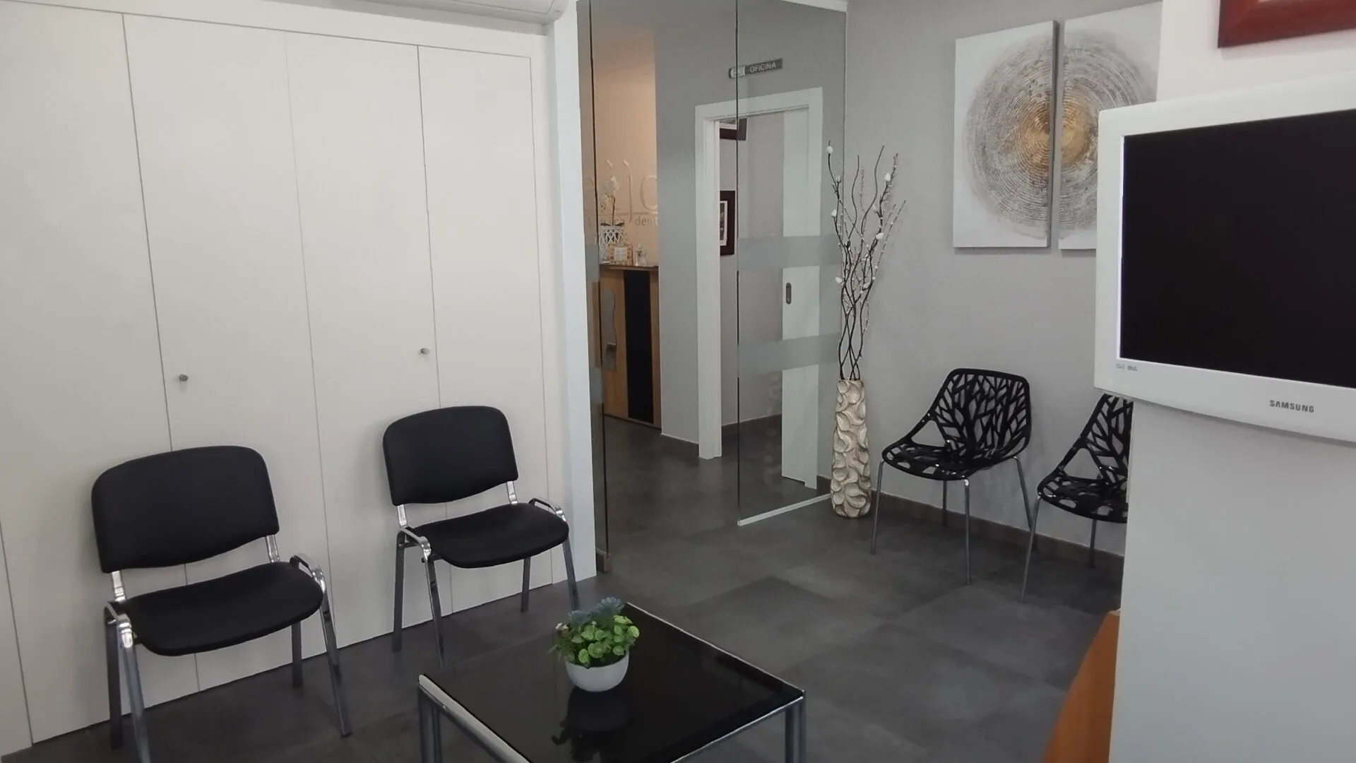Sala de espera de Clínica Dental Seijo con butacas negras y acceso acristalado a recepción