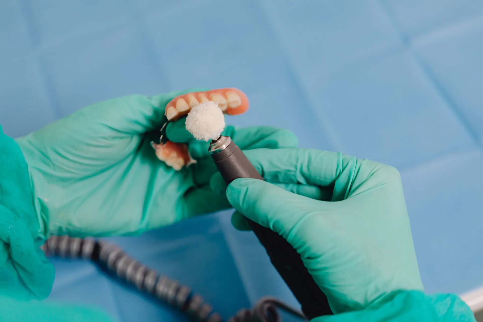 Manos con guantes puliendo una prótesis dental removible en la clínica