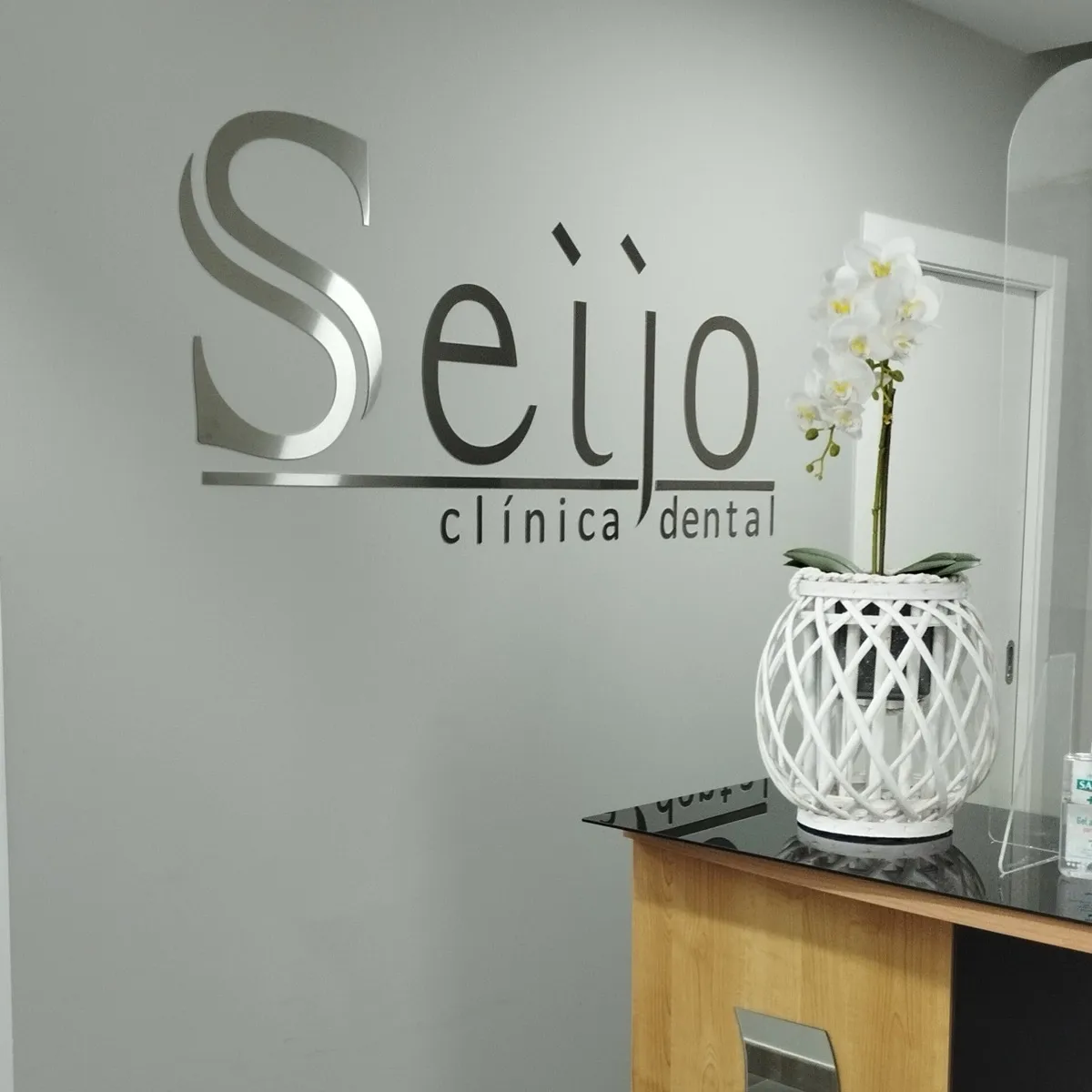 Recepción de Clínica Dental Seijo con el rótulo de la clínica en la pared y una orquídea
